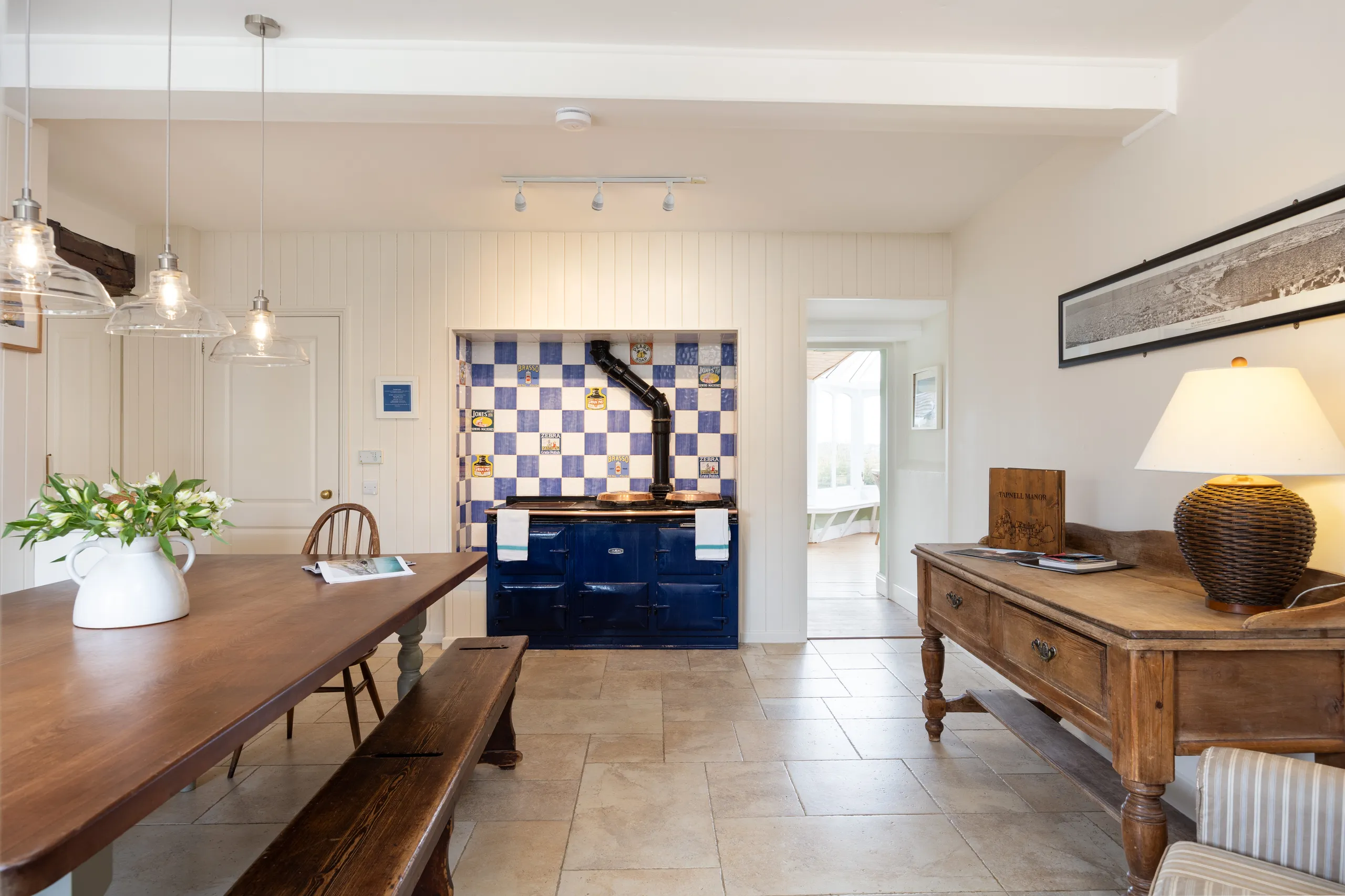 Rustic manor kitchen with wooden dining table, pendant lights and a blue range cooker against a blue-and-white tiled splashback