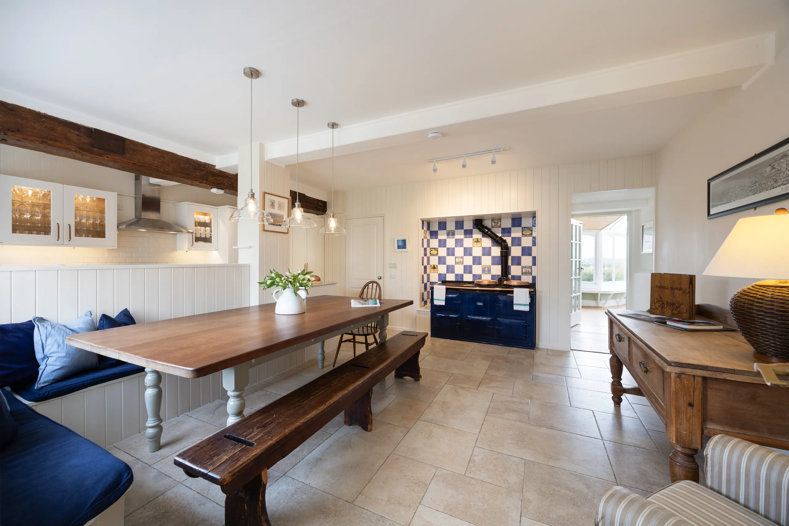Spacious country kitchen with wooden dining table, bench seating and navy range cooker with blue and white tiled surround
