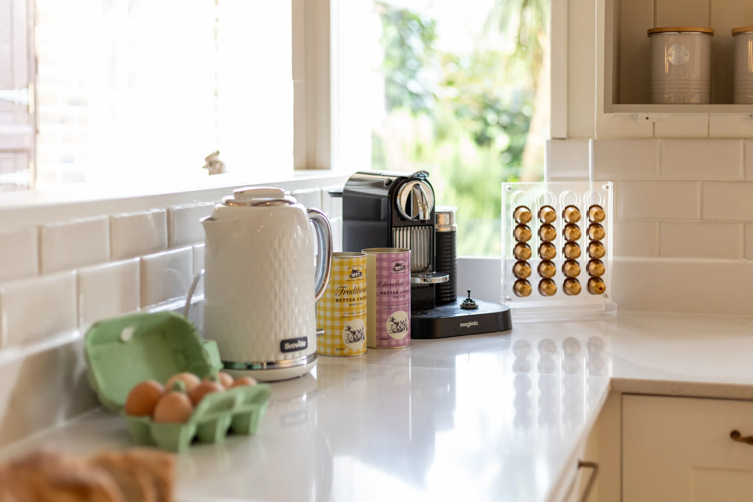 Bright kitchen worktop with kettle, coffee machine and pod rack by a sunlit window