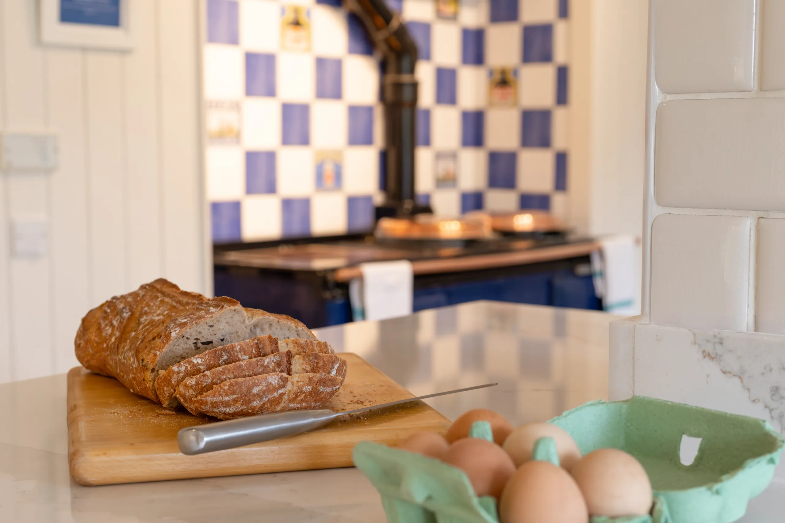 Sliced loaf of bread on a chopping board with a knife, beside a carton of eggs in a country kitchen