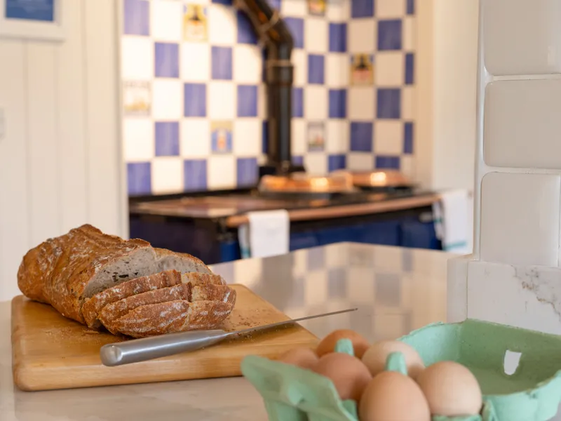 Sliced loaf of bread on a chopping board with a knife, beside a carton of eggs in a country kitchen
