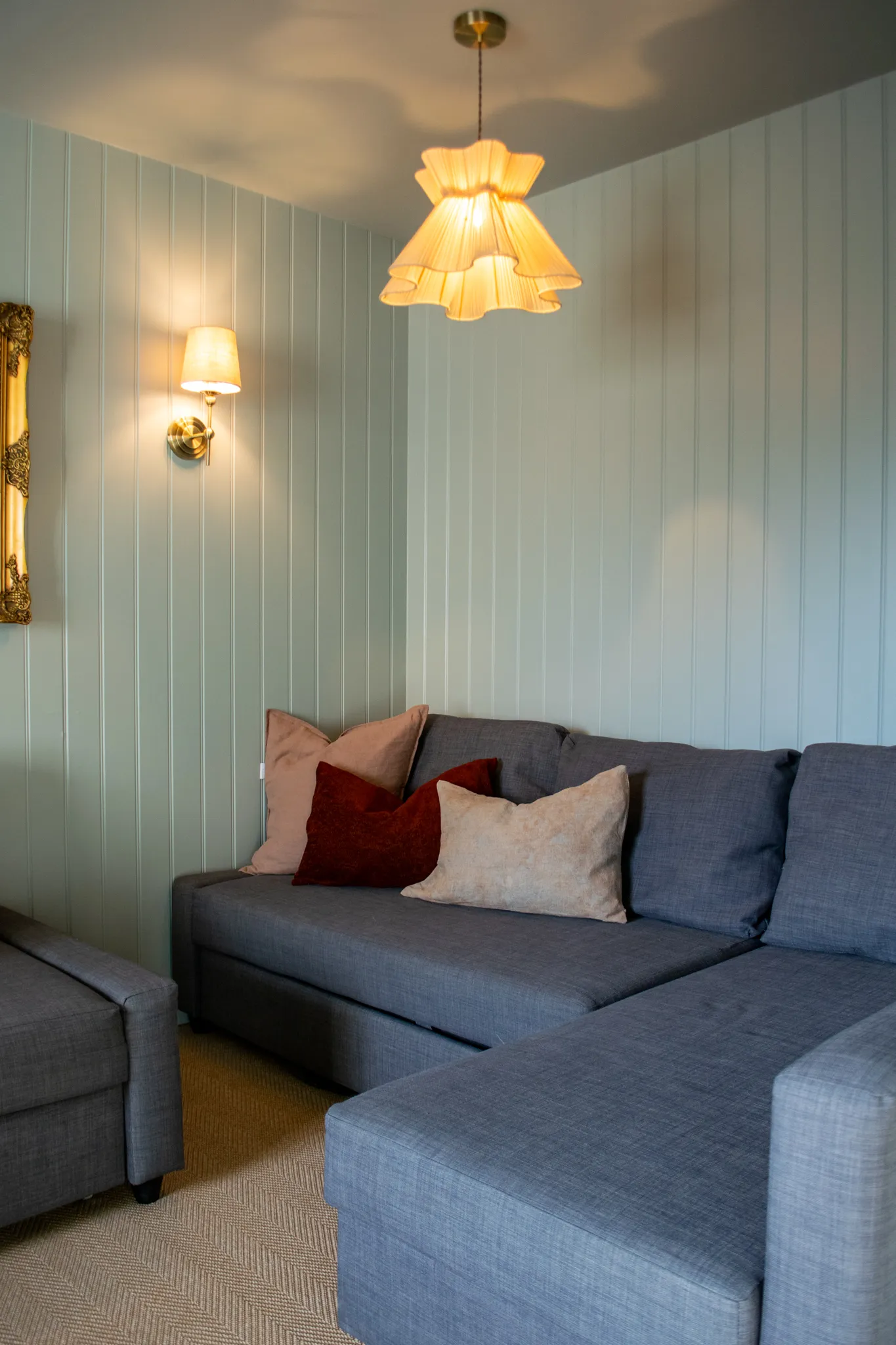 Cosy snug with blue panelled walls, grey corner sofa and warm pendant lighting