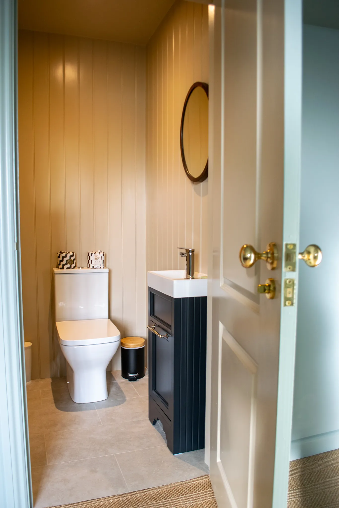 Compact cloakroom with white toilet, navy vanity unit and round mirror