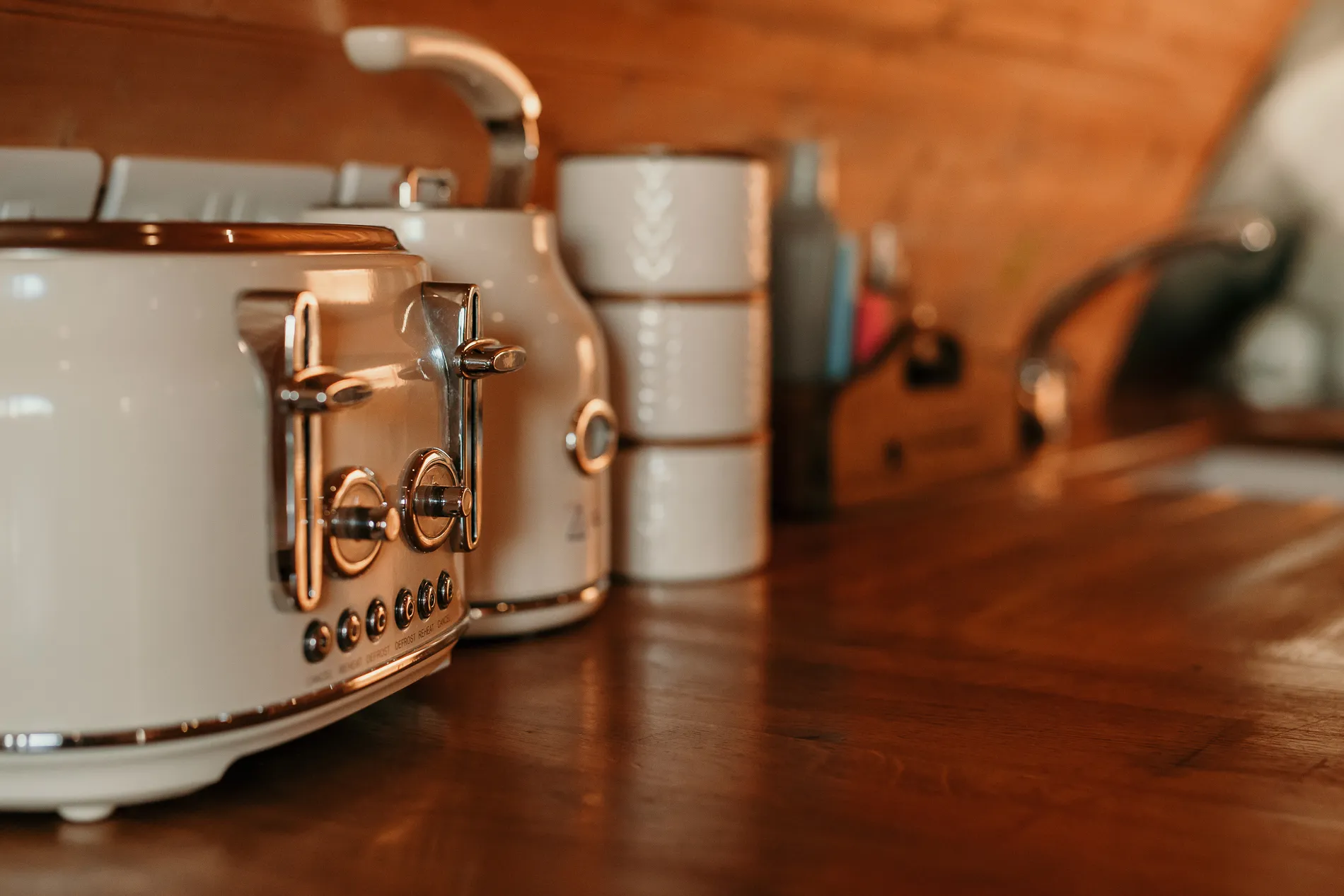 Close-up of a cream toaster and matching kettle on a wooden kitchen worktop with stacked white bowls in the background