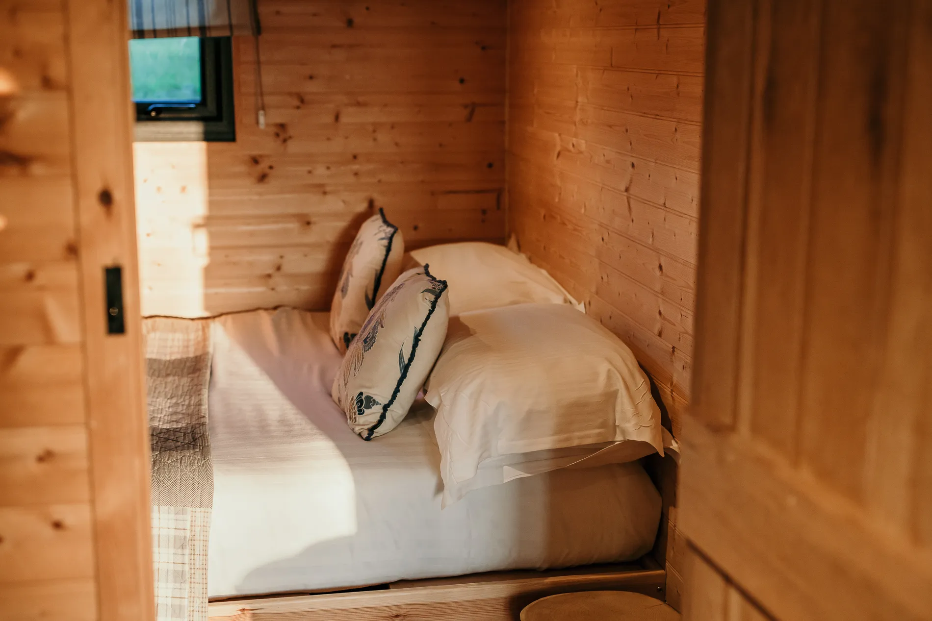 Cosy wooden cabin bedroom with a neatly made bed and patterned cushions in warm sunlight