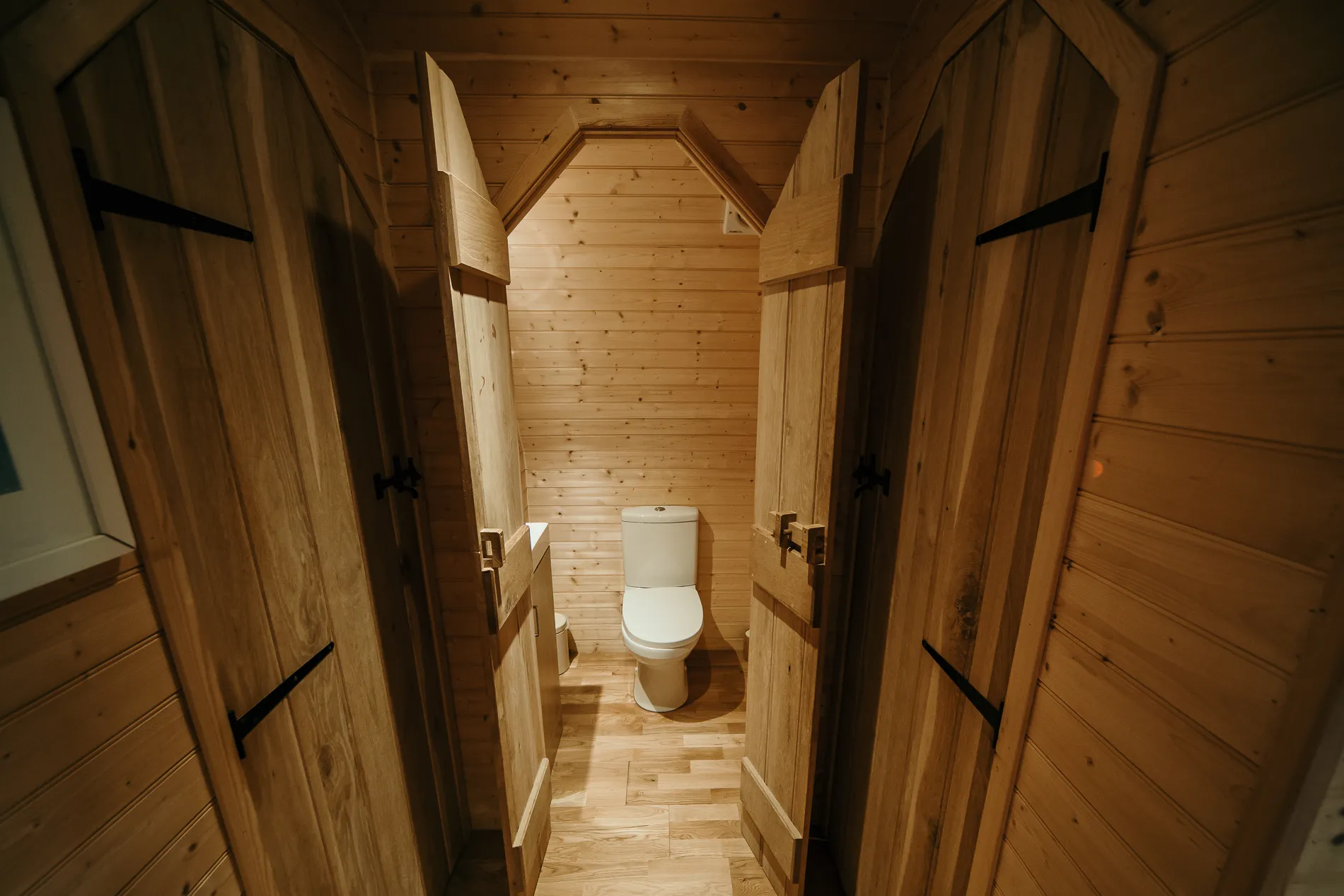 Wood-panelled bathroom with open timber doors and toilet in a cabin-style interior