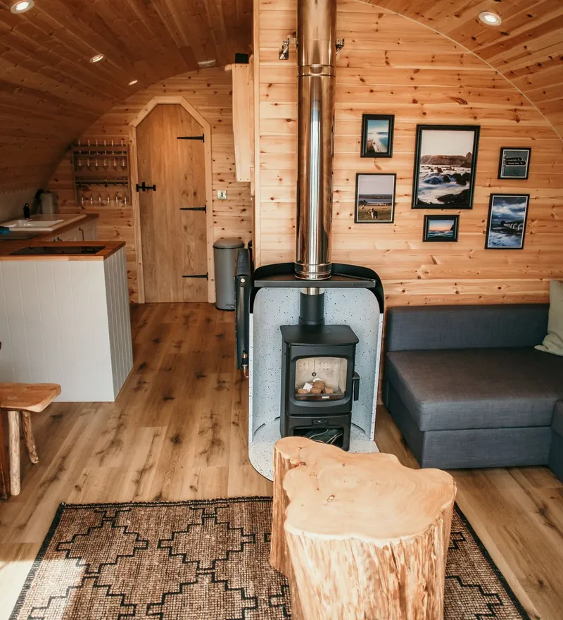 Cosy wooden cabin interior with wood-burning stove, kitchenette and grey corner sofa