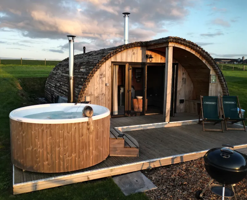 Cosy wooden glamping pod with outdoor hot tub on a deck at sunset