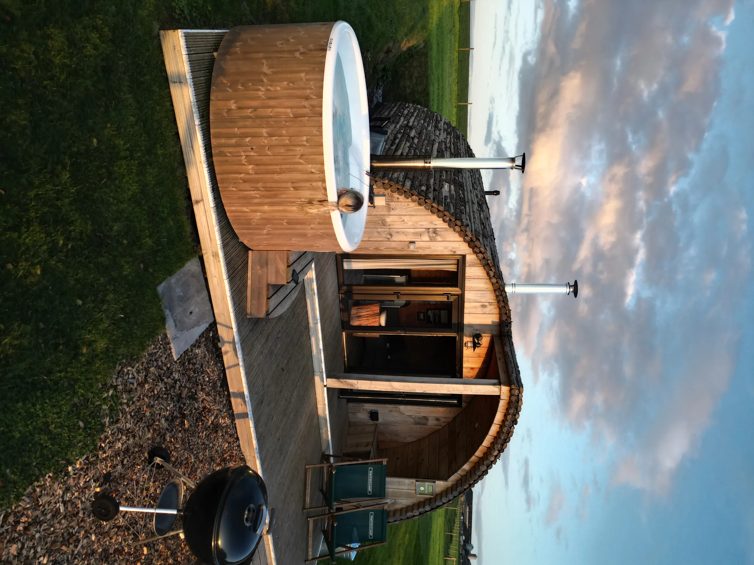 Cosy wooden glamping pod with outdoor hot tub on a deck at sunset