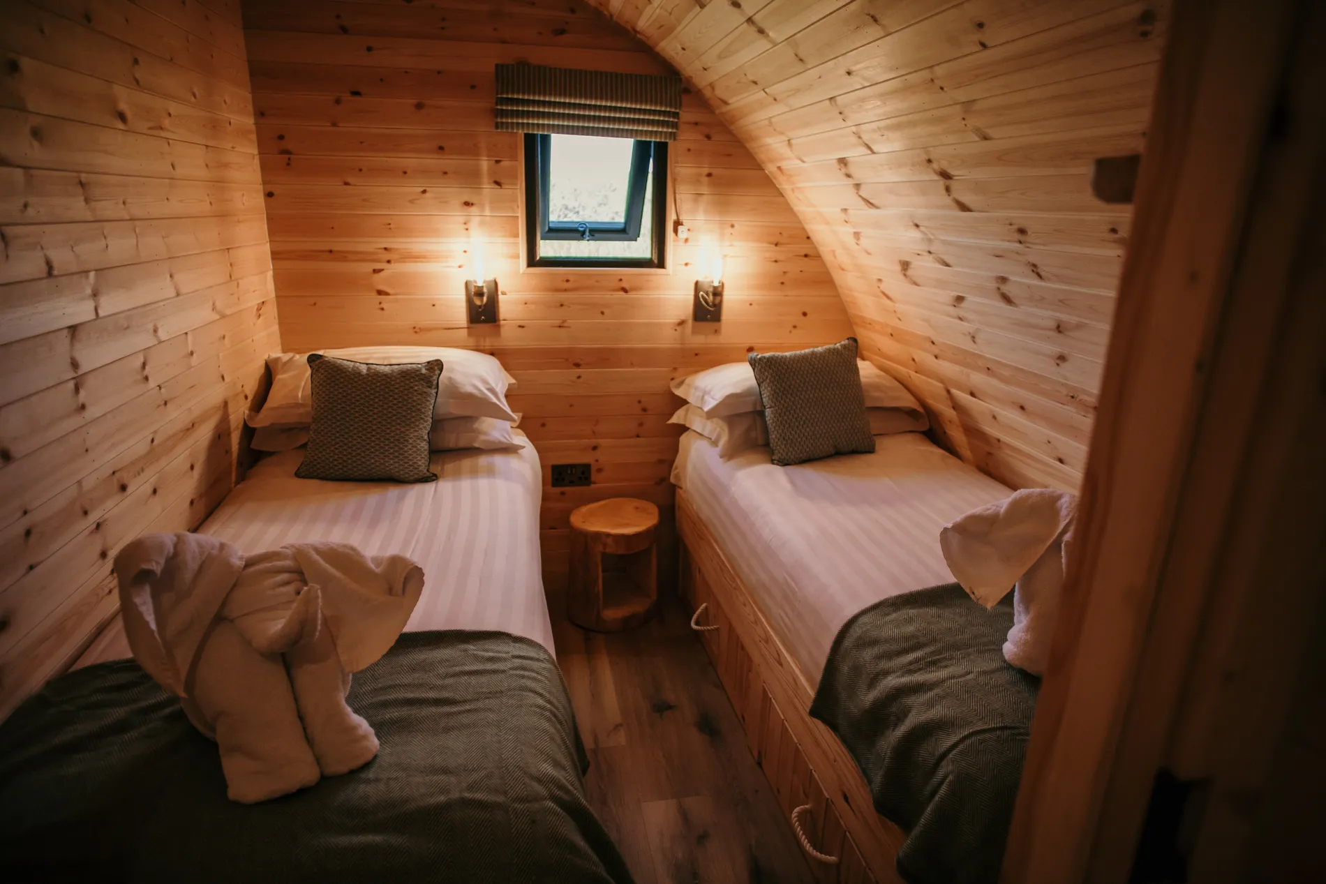 Cosy wooden cabin bedroom with two single beds, bedside lights and a small window