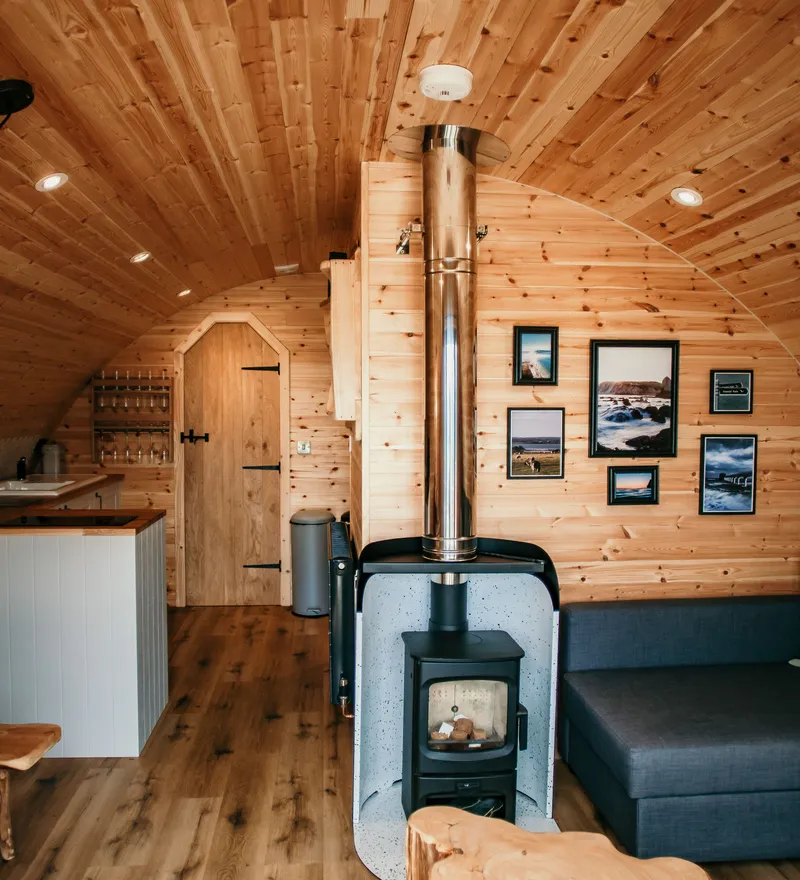Cosy wooden cabin interior with a wood-burning stove, kitchenette and grey sofa
