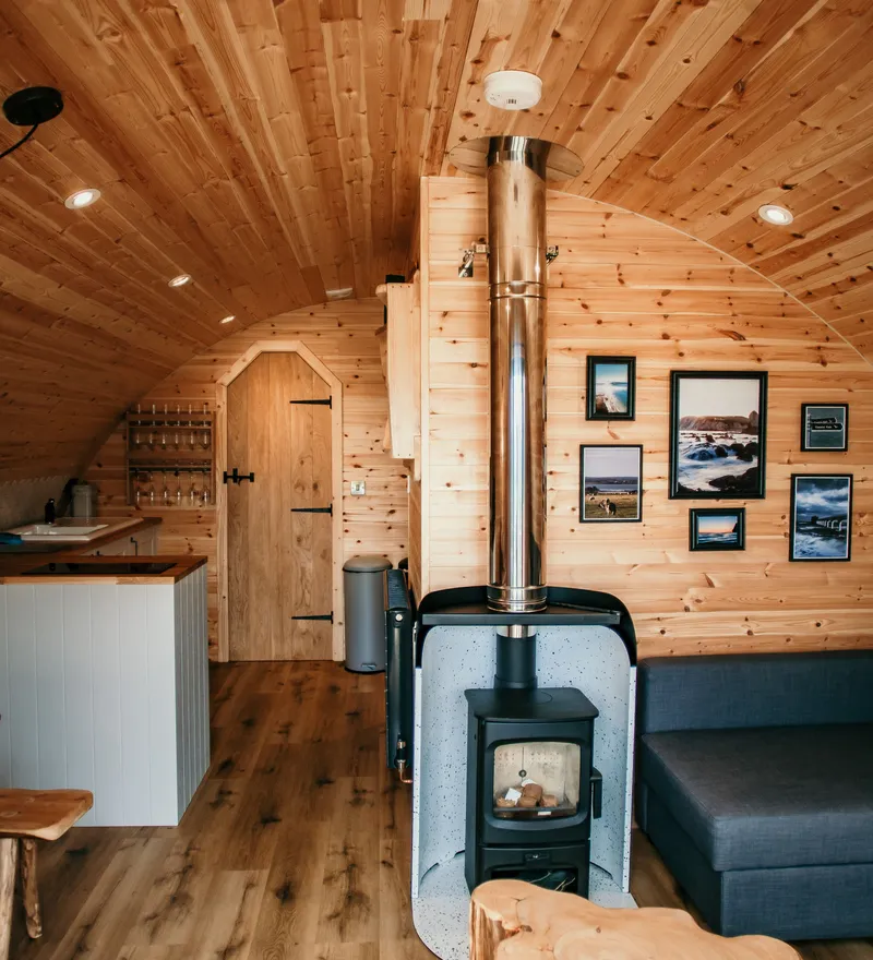 Cosy wooden cabin interior with a wood-burning stove, kitchenette and grey sofa