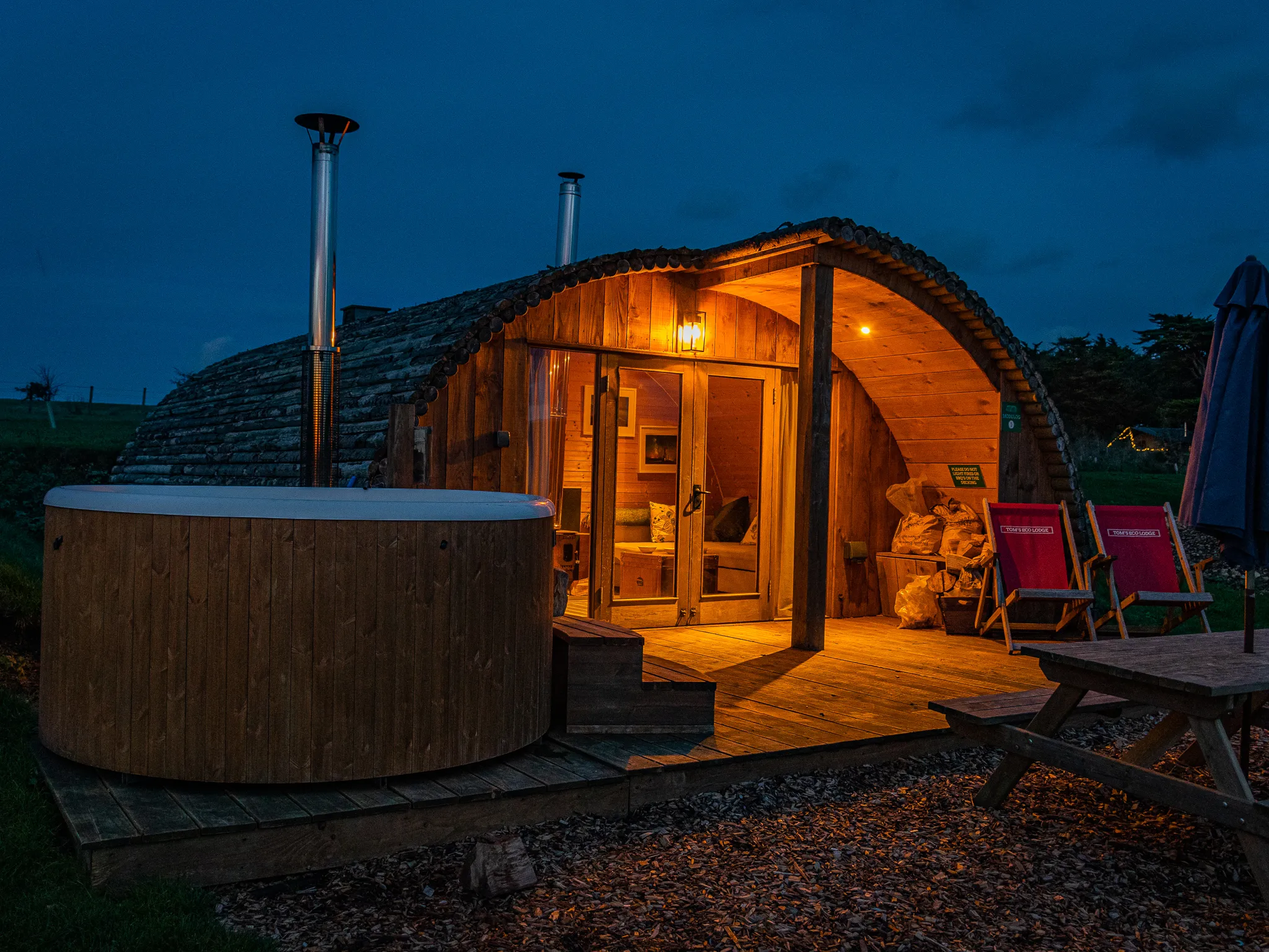 Cosy wooden glamping pod with hot tub on a deck at dusk