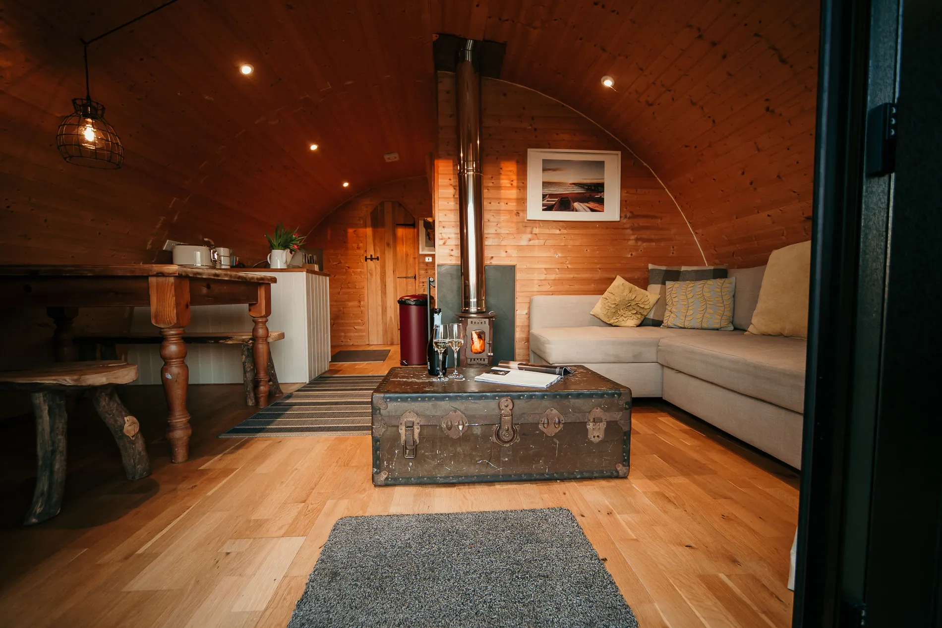 Cosy wooden cabin interior with a log burner, corner sofa and vintage trunk coffee table.