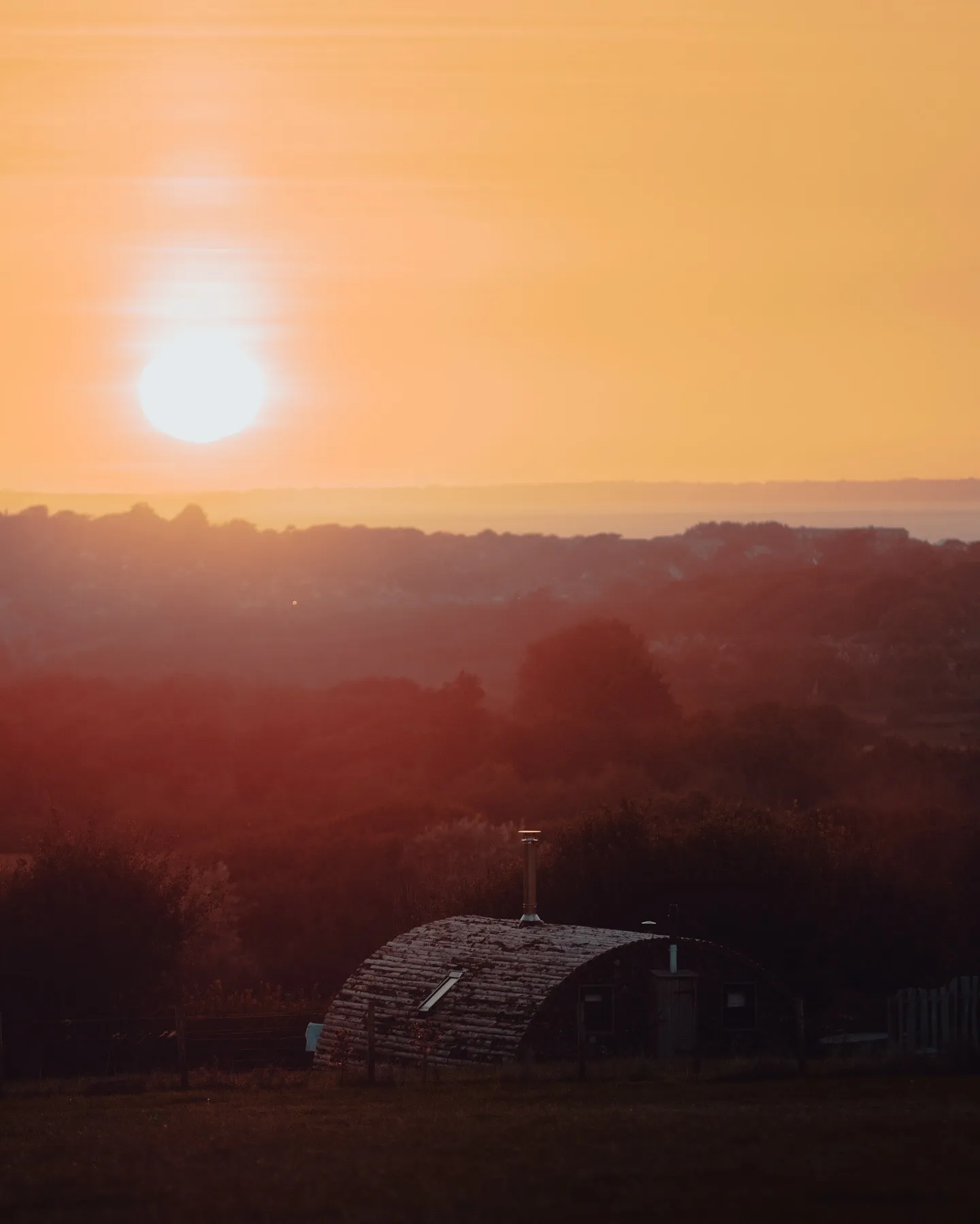 Sunset over rolling countryside with a small hut in the foreground