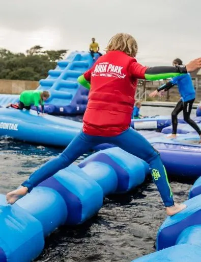 Children and adults playing on an inflatable aqua park obstacle course on water