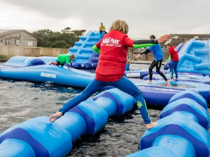 Children and adults playing on an inflatable aqua park obstacle course on water