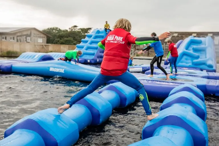 Children and adults playing on an inflatable aqua park obstacle course on water