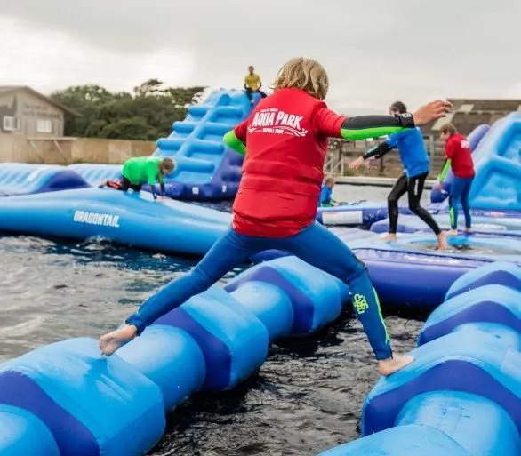 Children and adults playing on an inflatable aqua park obstacle course on water