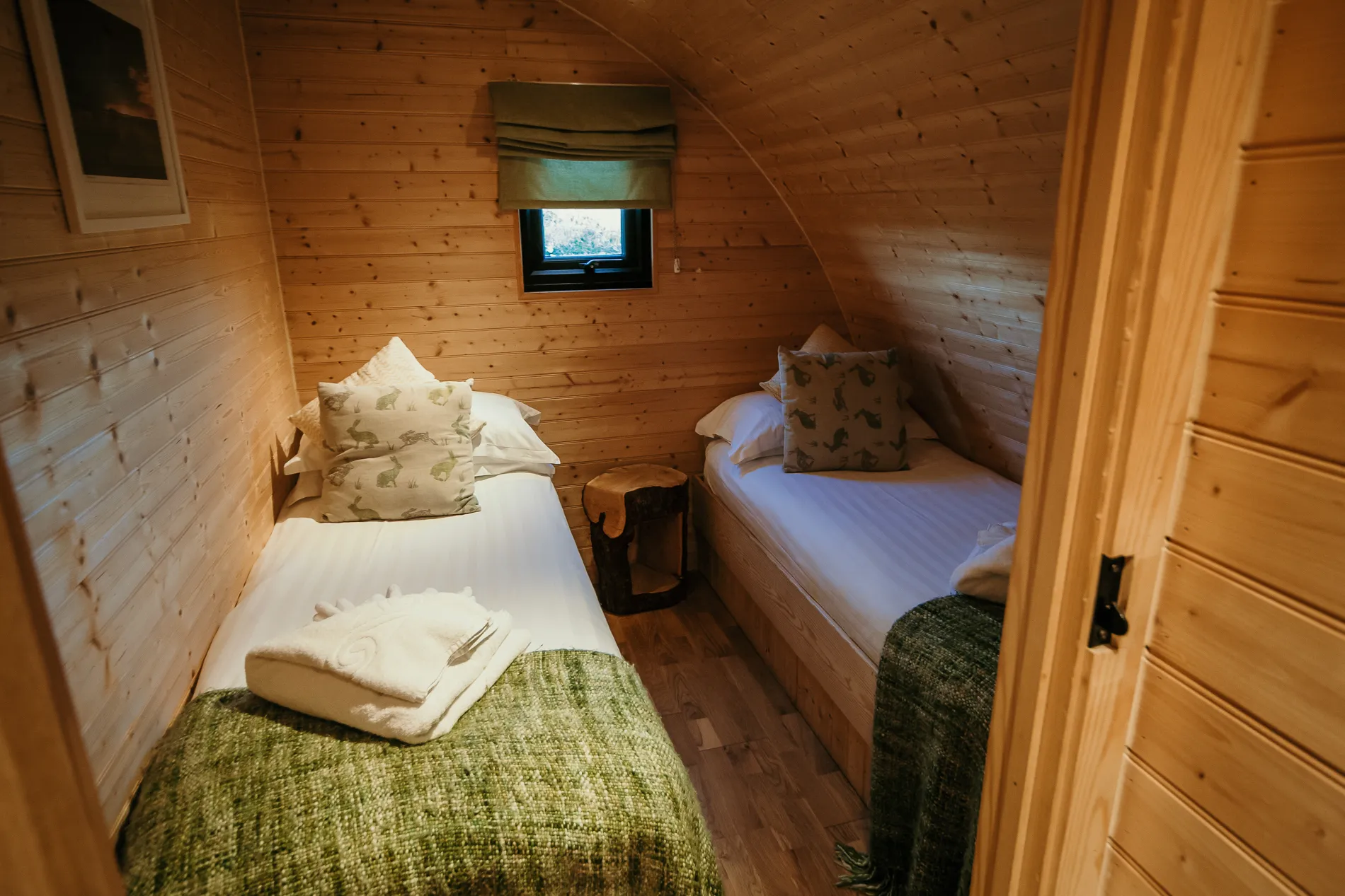 Cosy wooden cabin bedroom with two single beds, green throws and a small window