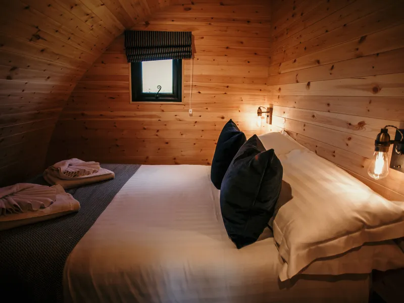 Cosy wooden cabin bedroom with double bed, folded towels, wall lights and small window