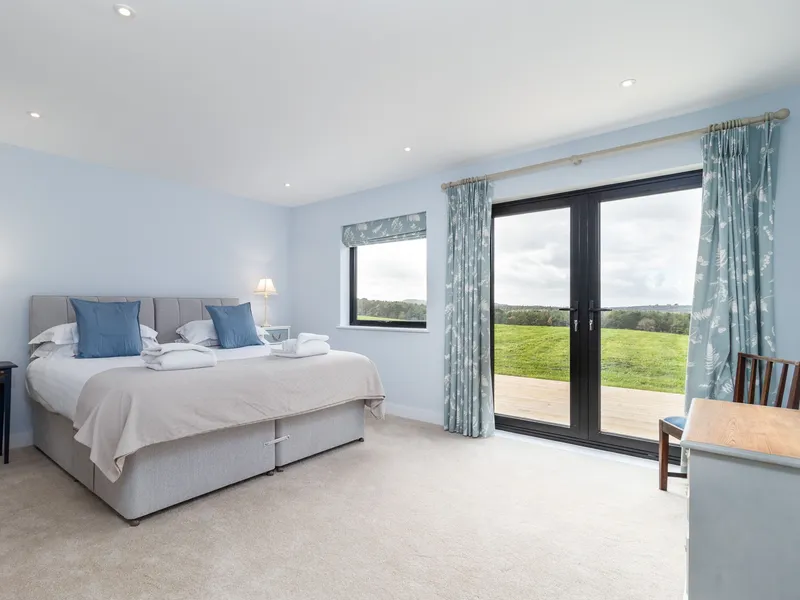 Light blue bedroom with double bed and patio doors opening to countryside views