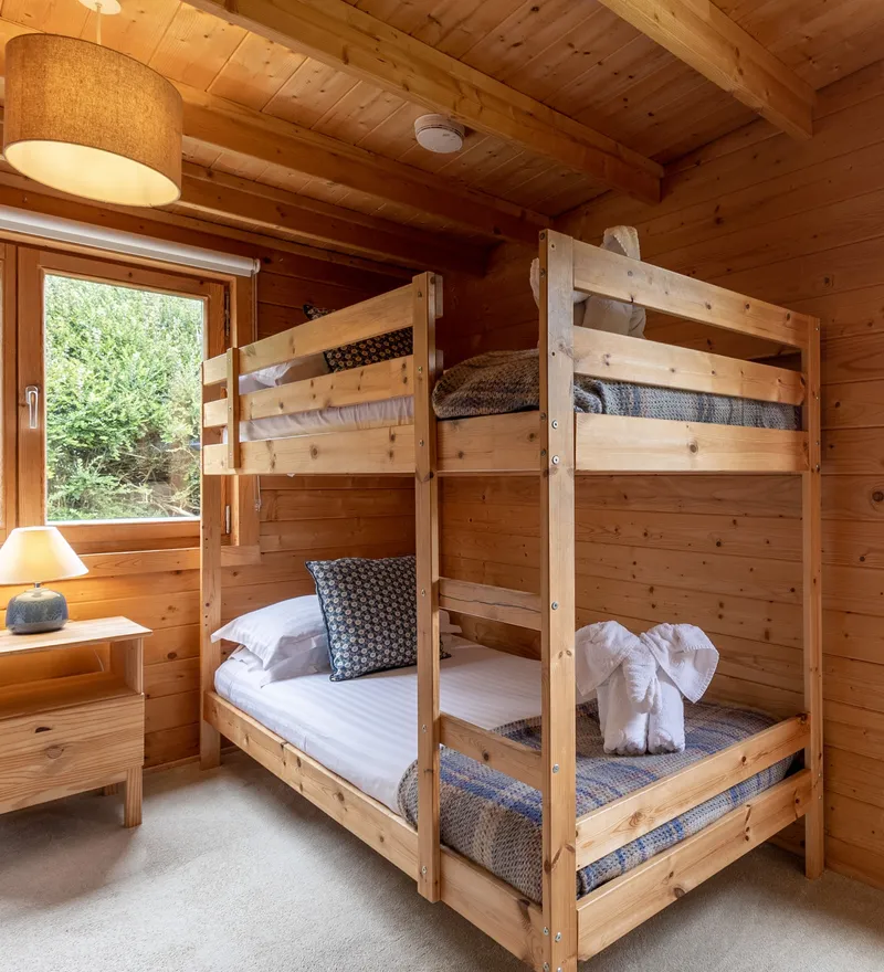 Cosy wooden cabin bedroom with bunk beds and bedside table by large windows