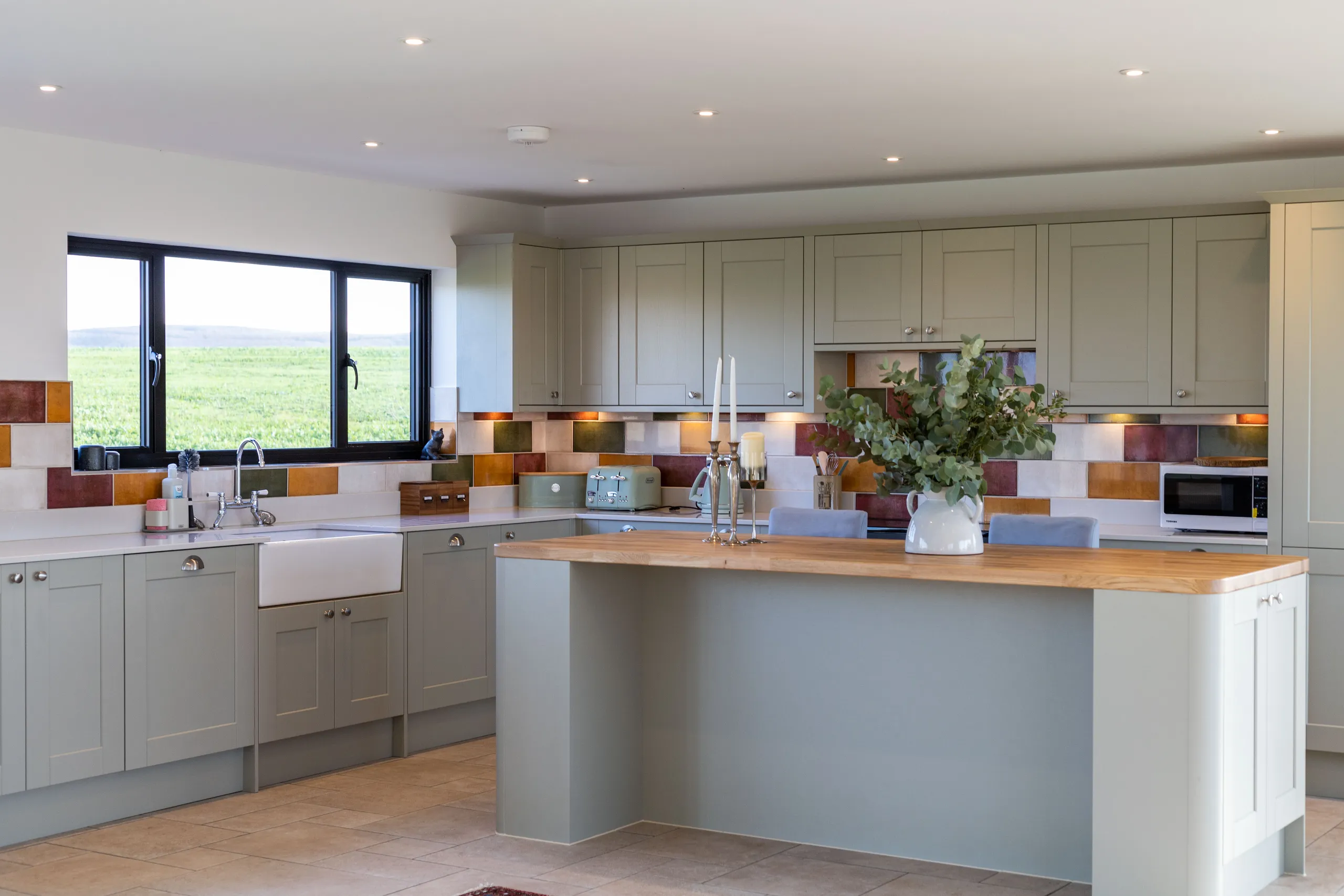 Modern country kitchen with sage-grey cabinets, wooden island and colourful tiled splashback