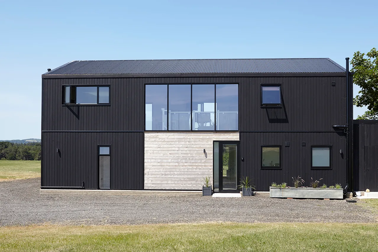 Front elevation of a modern black-clad house with large central windows and timber cladding around the entrance