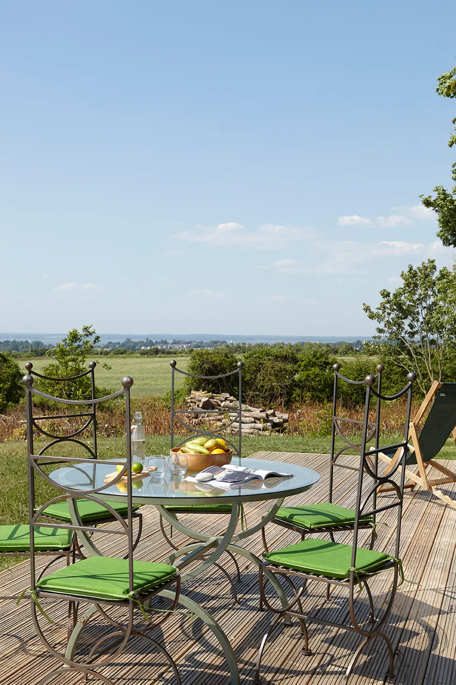 Outdoor patio table and four chairs with green cushions overlooking countryside fields