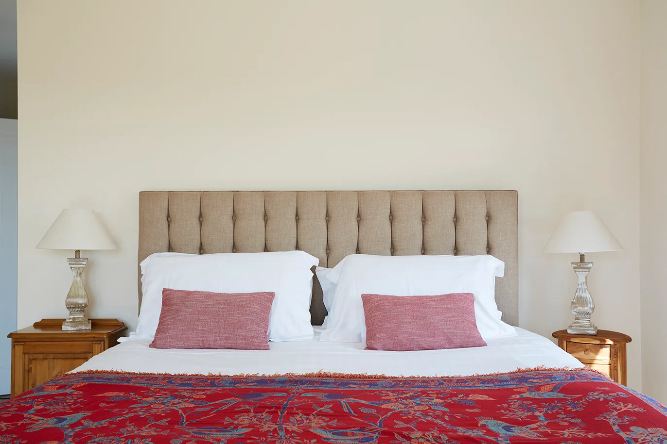 Neutral bedroom with tufted headboard, white bedding, pink cushions and red patterned throw