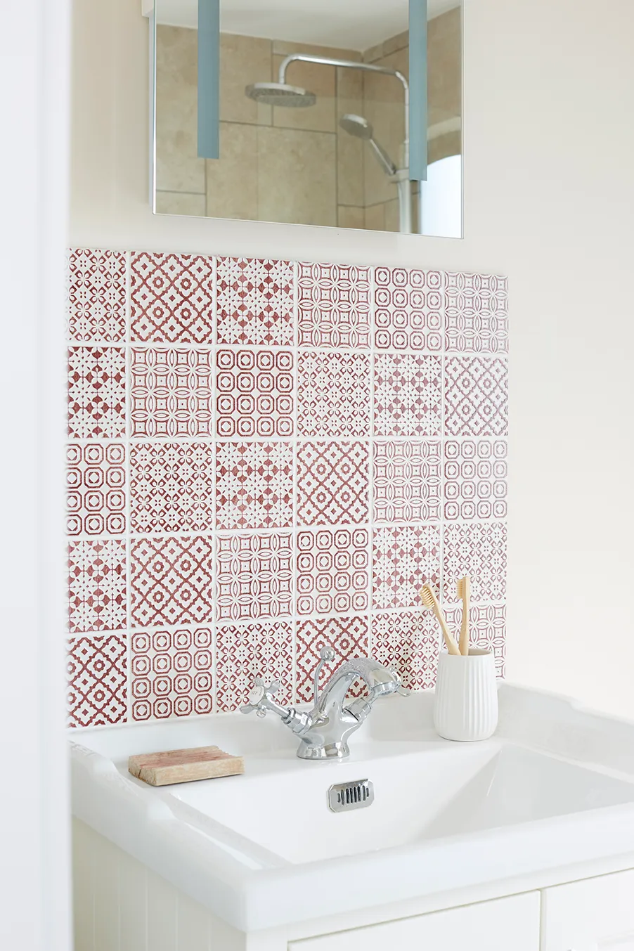 Bathroom washbasin with chrome tap and red patterned tile splashback beneath a mirror