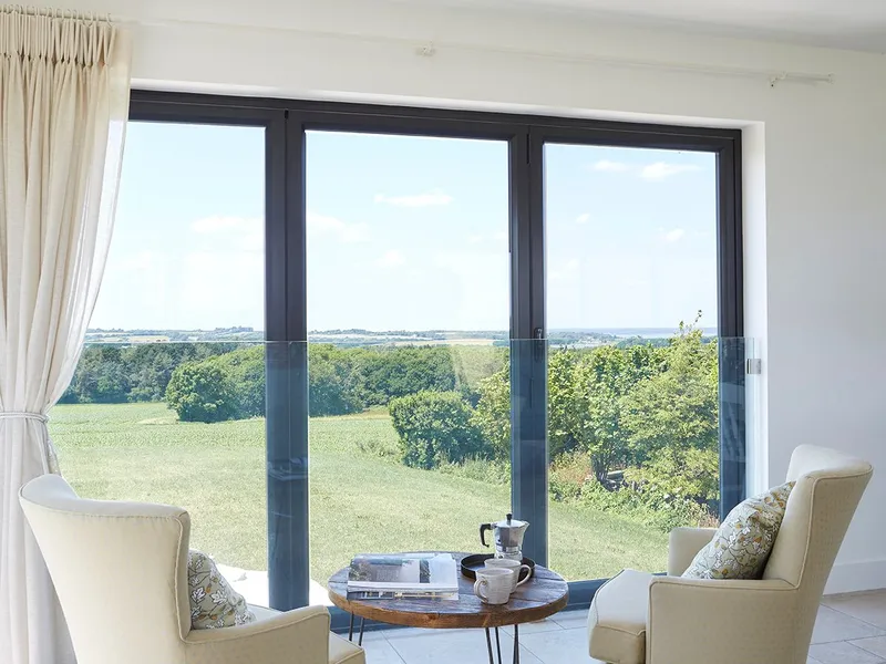 Cosy seating area with two cream armchairs and a coffee table by large sliding glass doors overlooking countryside
