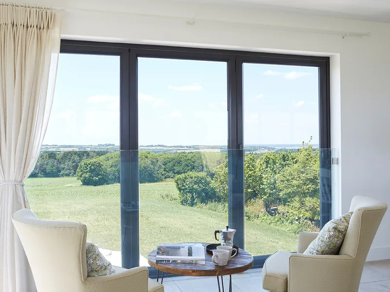 Cosy seating area with two cream armchairs and a coffee table by large sliding glass doors overlooking countryside