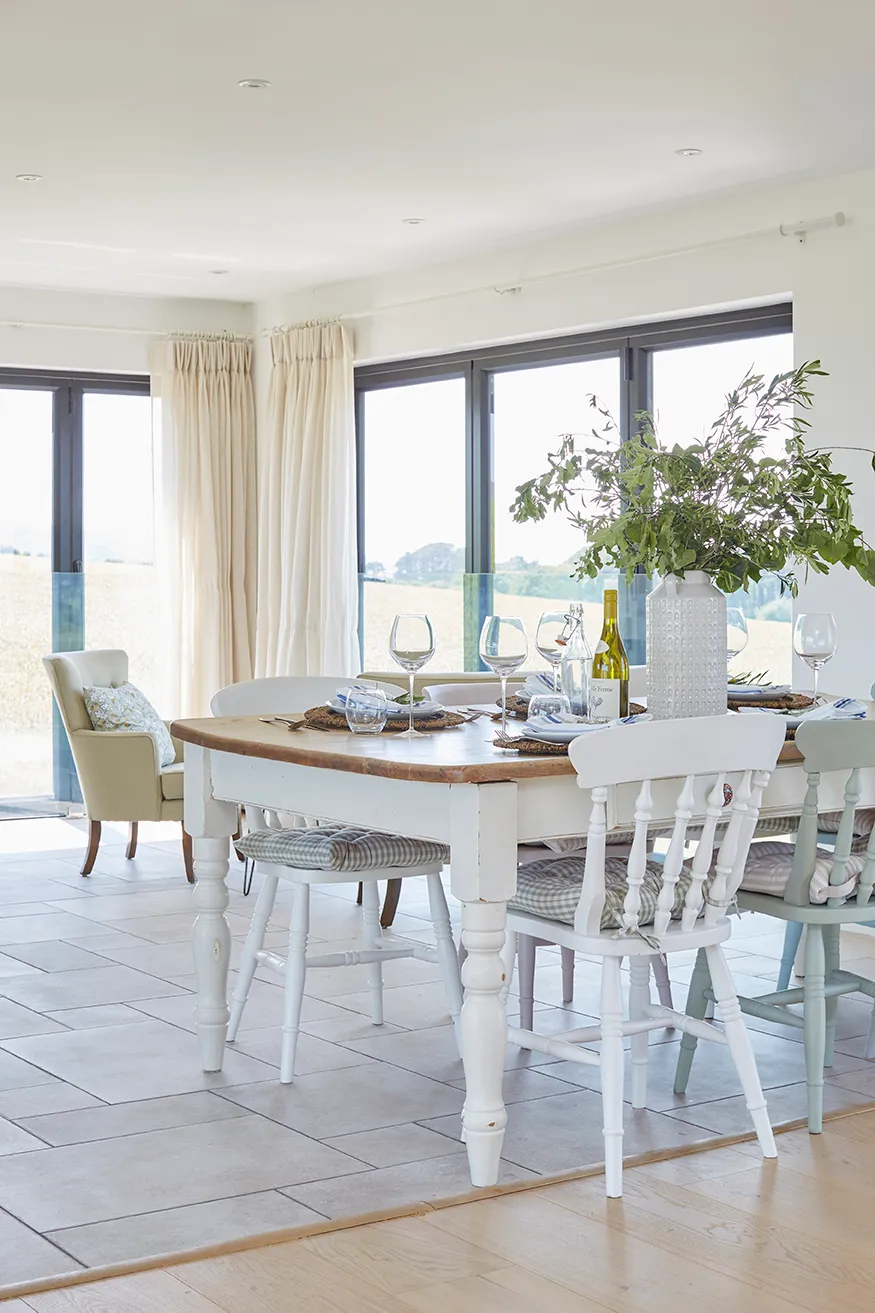 Bright dining room with rustic wooden table and mismatched chairs by large corner windows