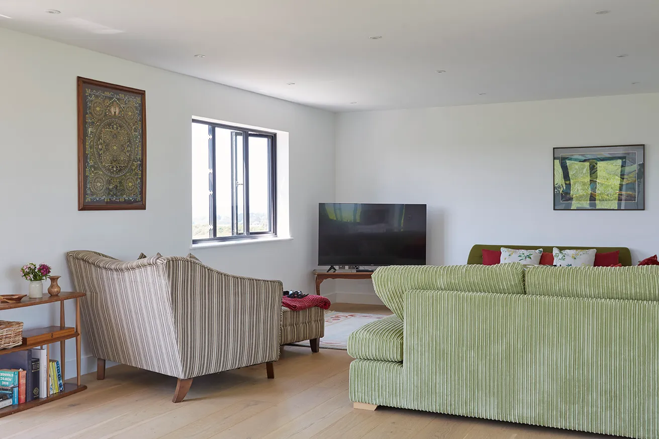 Bright, modern living room with striped armchairs, green sofa and TV by a window