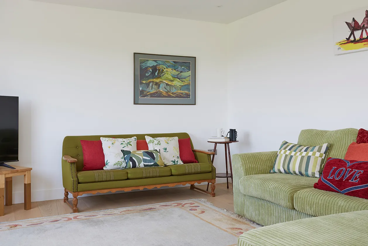 Bright sitting room with green sofas, patterned cushions and framed artwork on a white wall