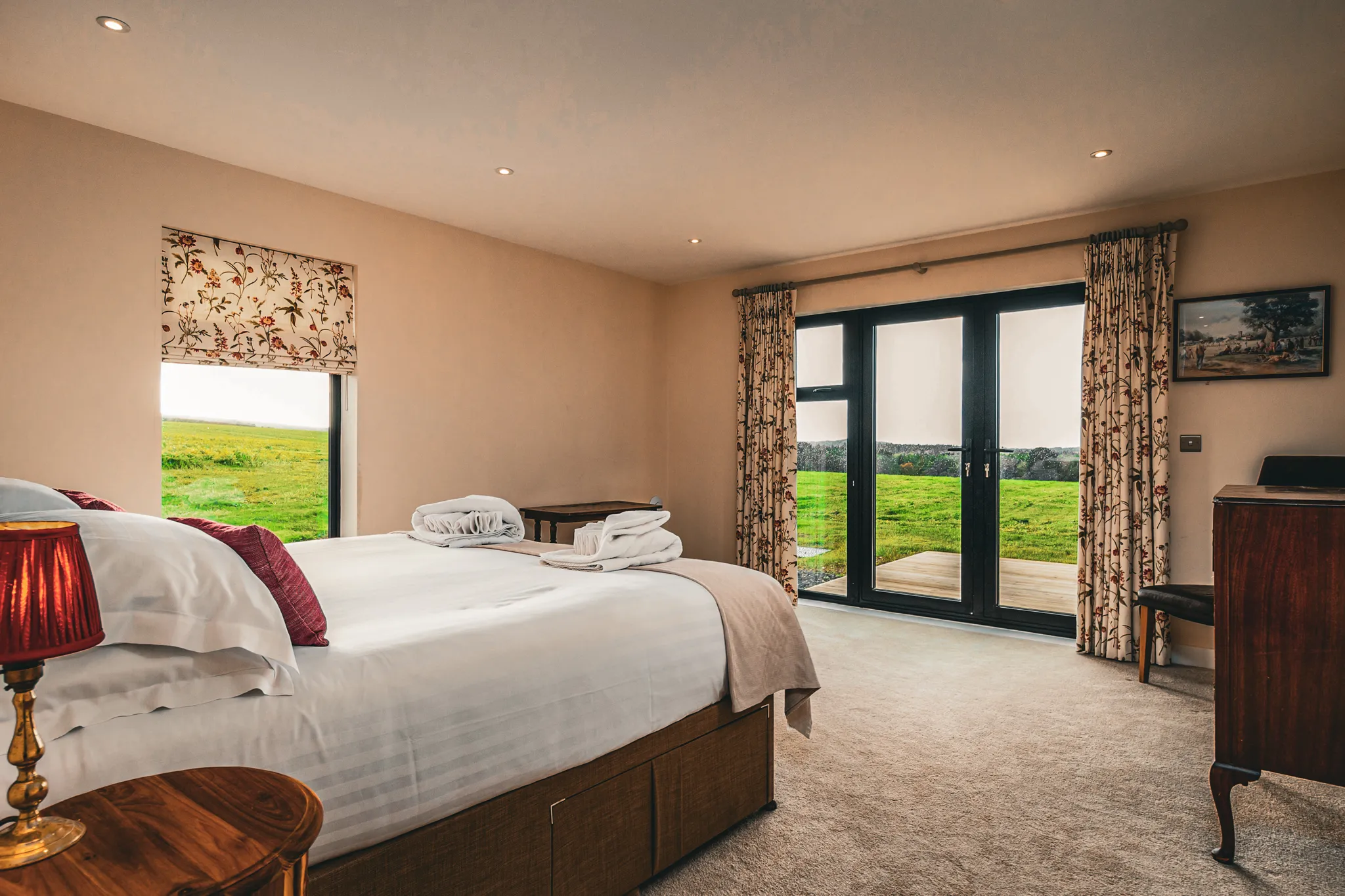 Cosy bedroom with double bed, floral curtains and French doors opening onto green countryside