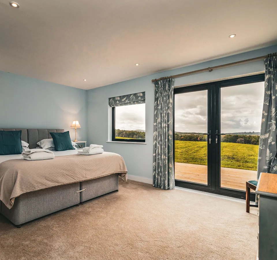 Cosy bedroom with double bed, bedside lamps and French doors opening onto countryside views
