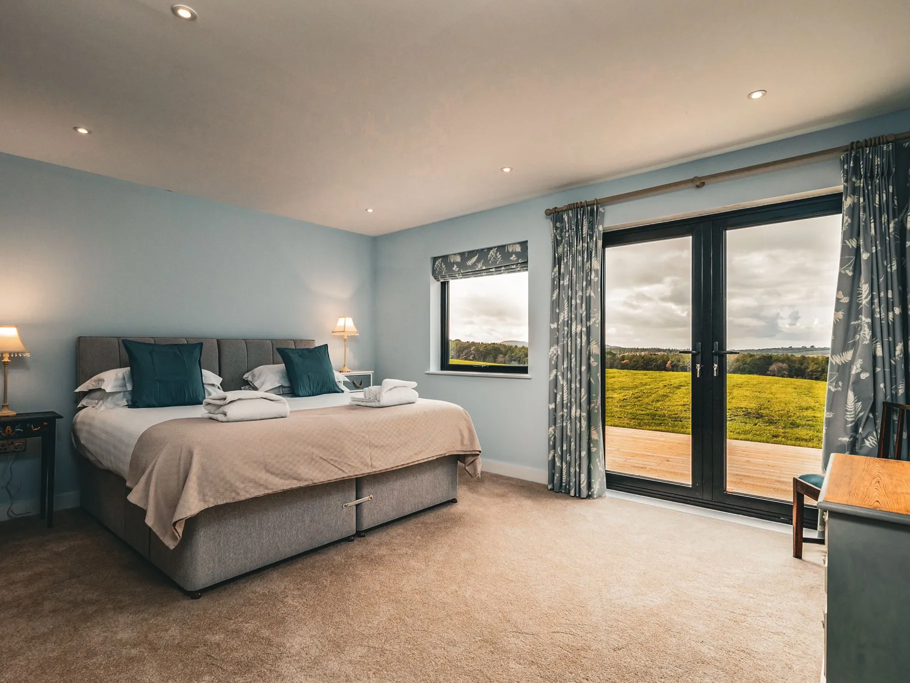Cosy bedroom with double bed, bedside lamps and French doors opening onto countryside views