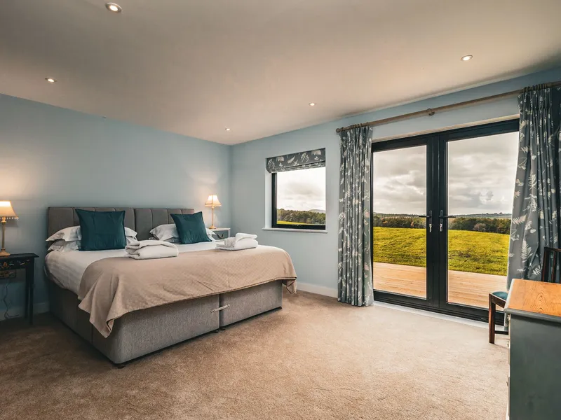 Cosy bedroom with double bed, bedside lamps and French doors opening onto countryside views