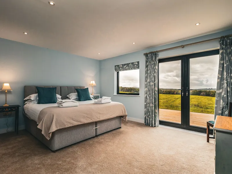Cosy bedroom with double bed, bedside lamps and French doors opening onto countryside views