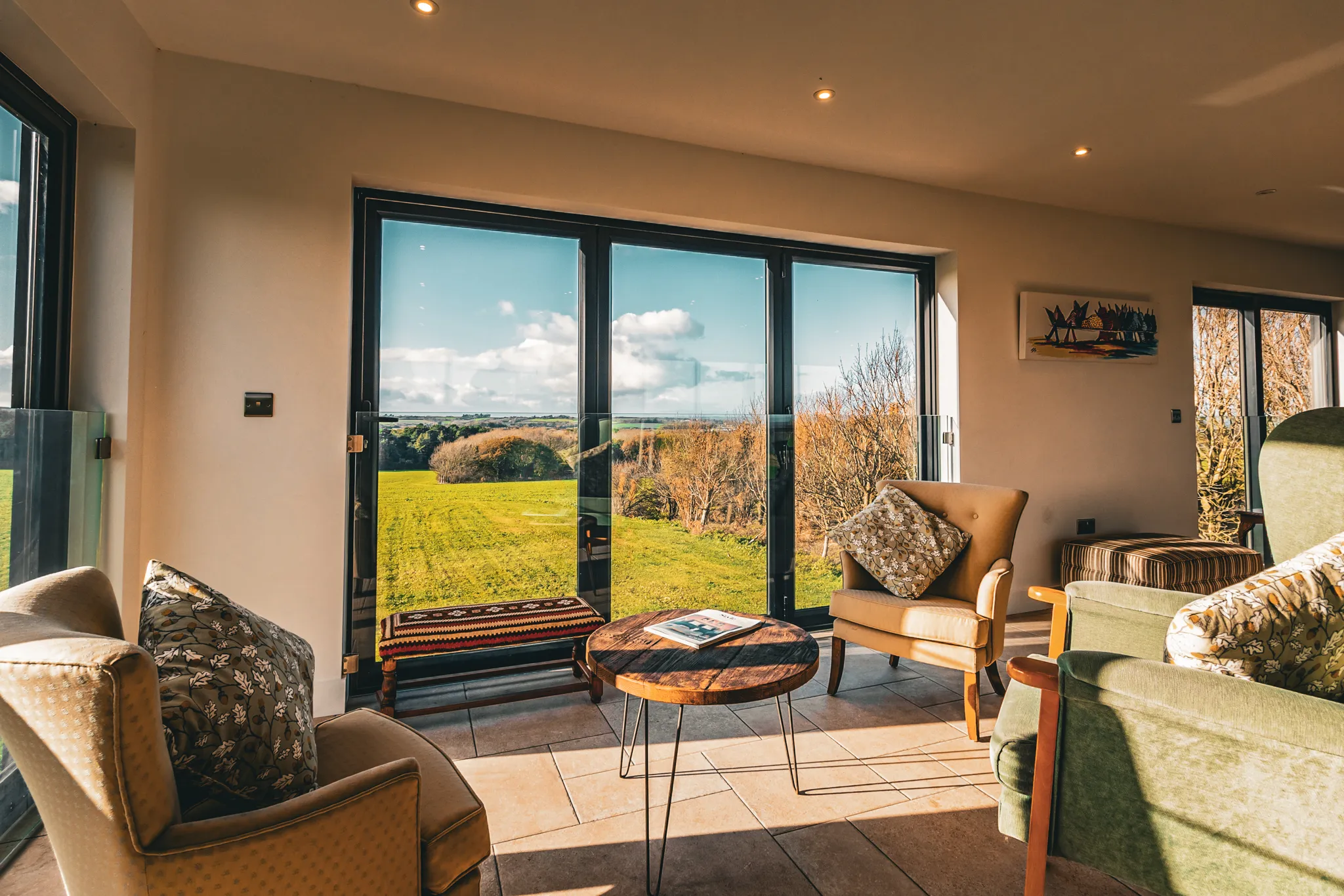 Cosy sitting area with armchairs and a coffee table beside large glass doors overlooking green countryside