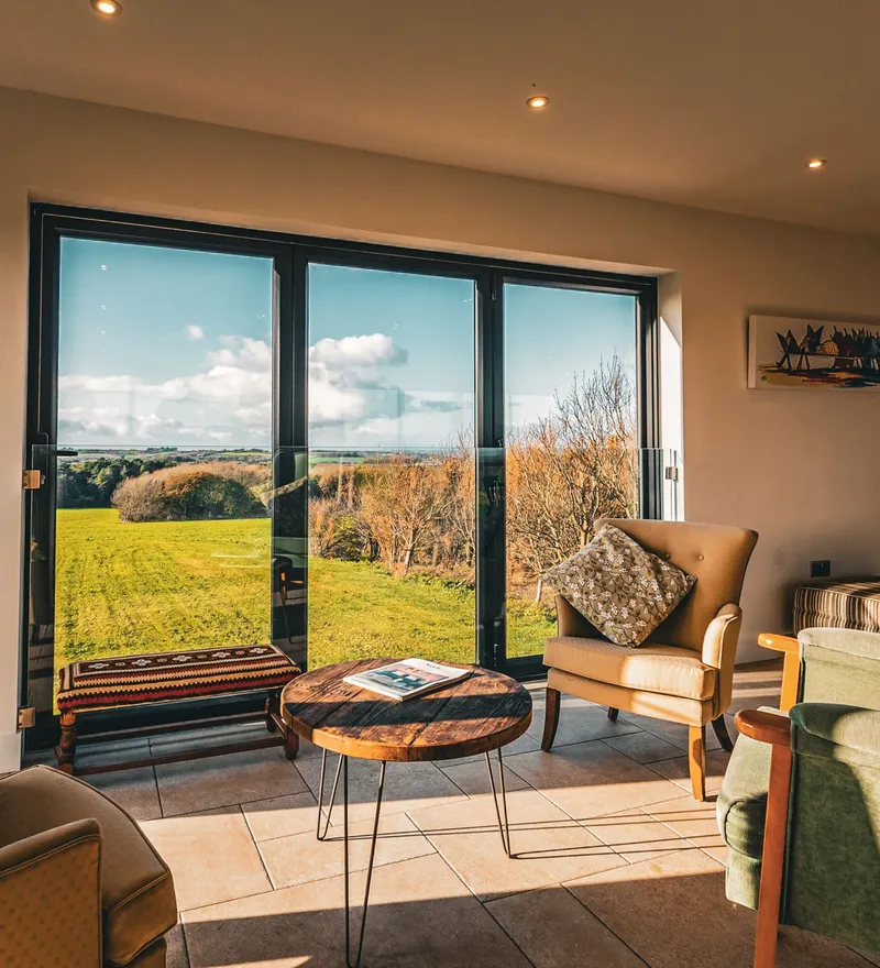 Cosy sitting area with armchairs and a coffee table beside large glass doors overlooking green countryside