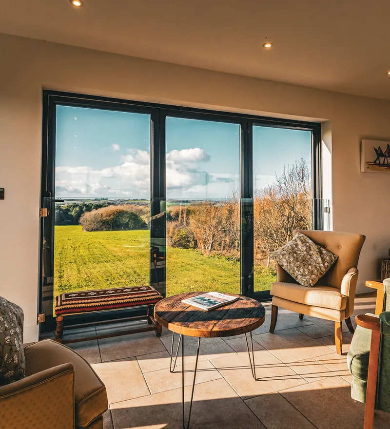 Cosy sitting area with armchairs and a coffee table beside large glass doors overlooking green countryside
