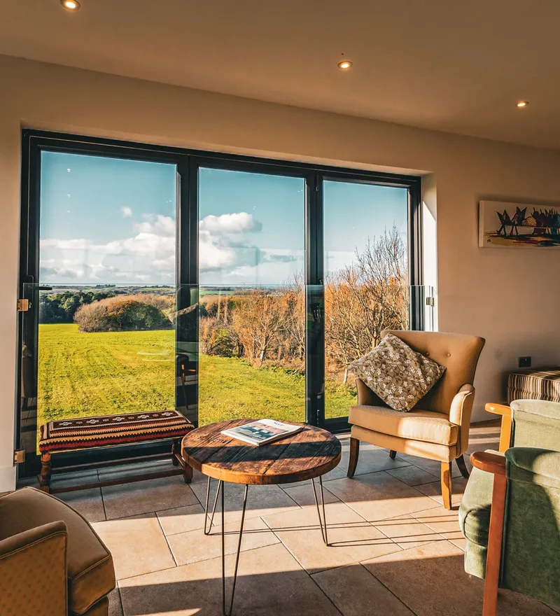 Cosy sitting area with armchairs and a coffee table beside large glass doors overlooking green countryside