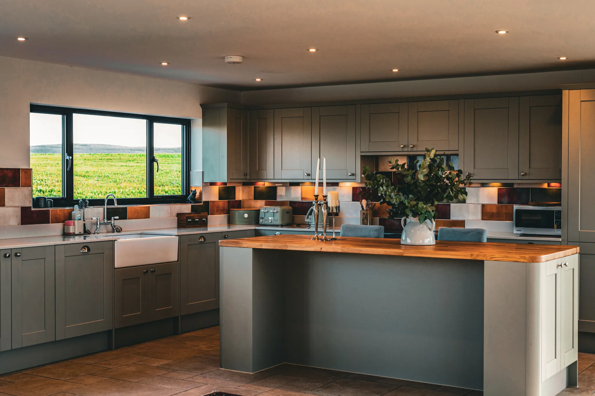 Modern grey kitchen with wooden island, farmhouse sink and large window overlooking green fields