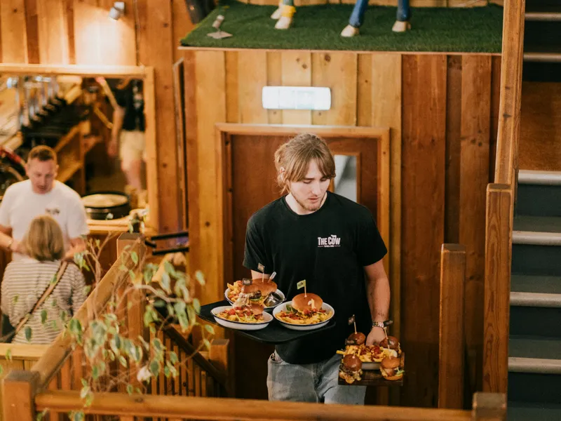 Restaurant staff member carrying trays of burgers and chips in a wood-panelled dining area