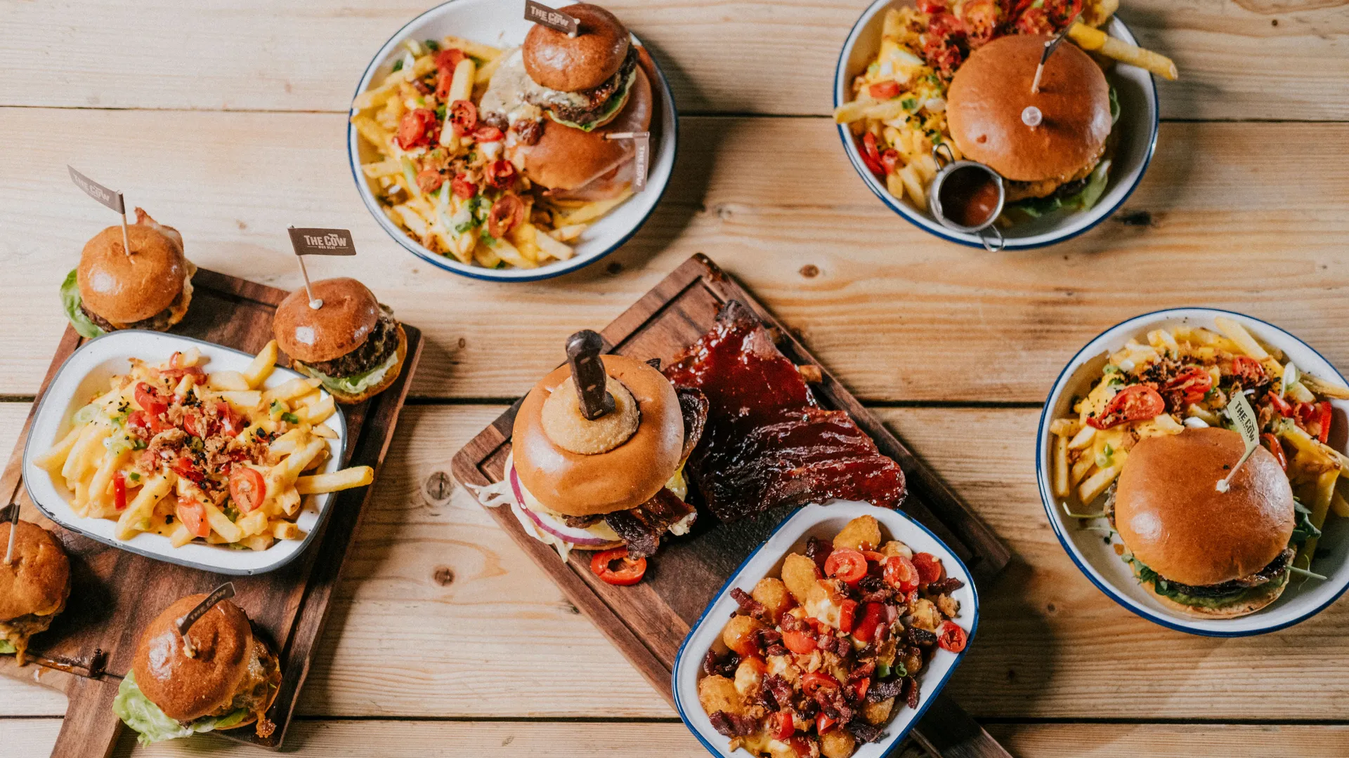 Assorted burgers and loaded chips served in enamel bowls on a wooden table