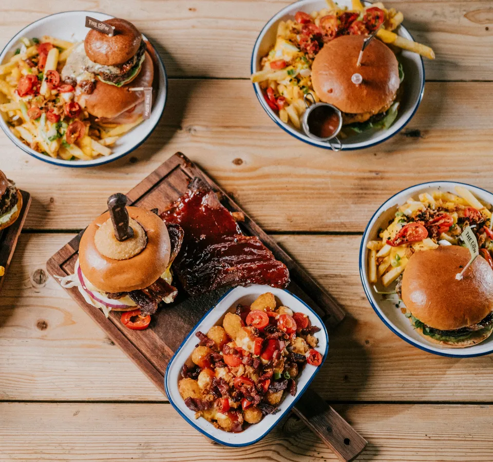 Assorted burgers and loaded chips served in enamel bowls on a wooden table